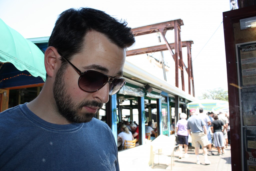 Rand attempts to look up restaurant reviews on his phone. Behind him: a line for one of the eateries. 