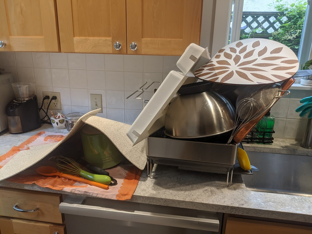 Pile of clean dishes stacked up next to a sink in a kitchen. 