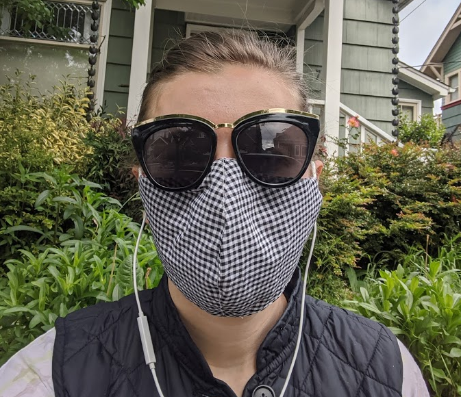 The author standing outside wearing a cloth face covering and dark sunglasses.