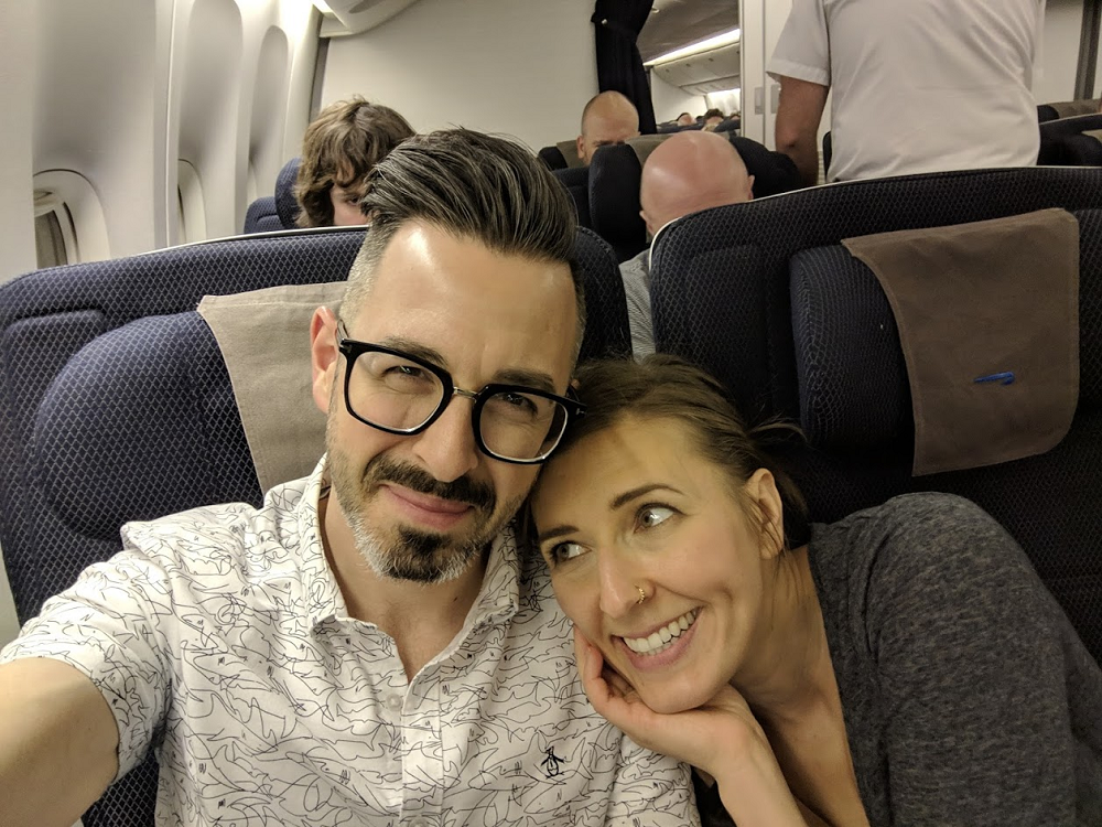 Man and woman cuddling together in the cabin of an airplane. The woman is looking up lovingly at the man. He is very handsome.