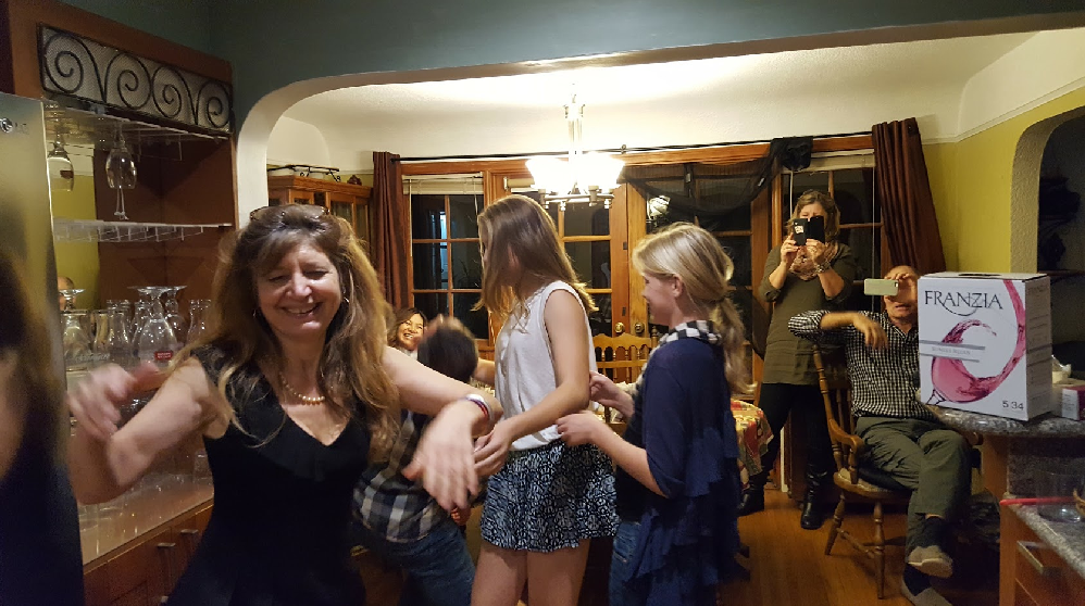 Family dancing in a kitchen, happily. There is box wine on the counter.