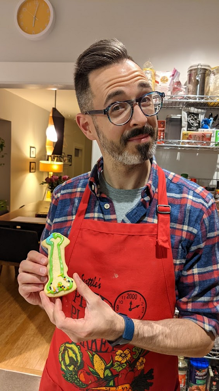 Rand is holding the decorated penis-shaped cookie. There are sprinkles on the balls.
