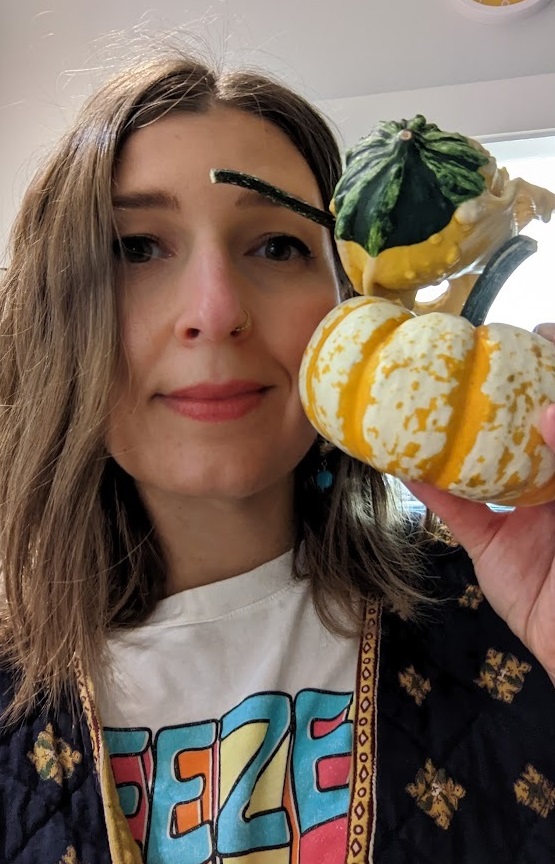Photo of the author holding two tiny gourds up close to her face and smiling at the camera. 